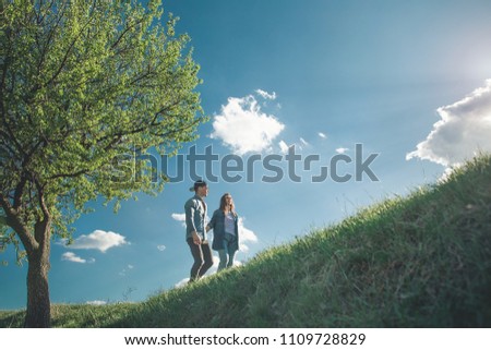 Low angle full length of affectionate girl and boy holding hands and climbing on top of green hill. They are enjoying amazing fresh air and pictorial nature around