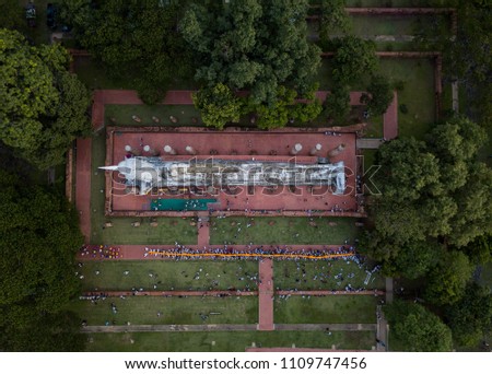 Aerial view of beautiful ancient Buddha statue with Buddhist monk and people hold a yellow rope walk around the big reclining Buddha statue. Top view from drone. 