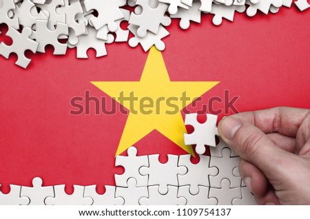 Vietnam flag  is depicted on a table on which the human hand folds a puzzle of white color