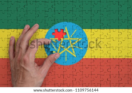 Ethiopia flag  is depicted on a puzzle, which the man's hand completes to fold