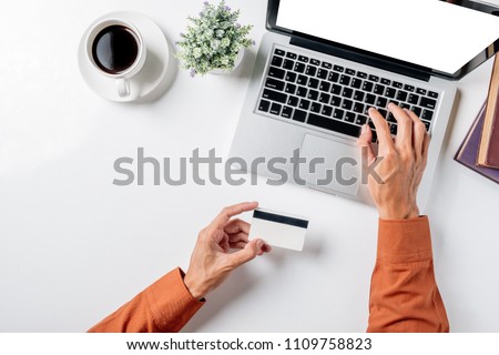 Man hand holding credit card and using laptop on white desk table with a lot of things.Top view with copy space,Flat lay.