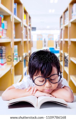 Picture of cute schoolgirl reading a textbook while sitting in the library