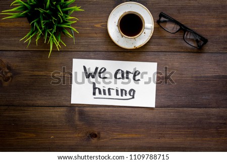 Search for worker, employee concept. We are hiring lettering on work desk on dark wooden background top view copy space
