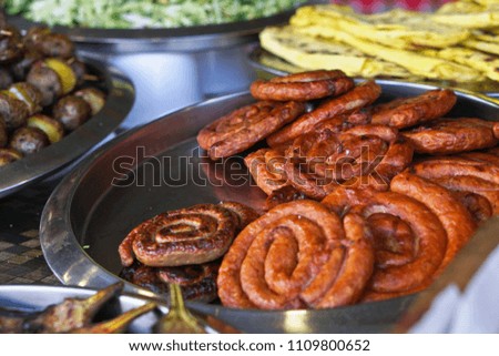 Grilled sausage on a grill with a delicious crust on the background of vegetables. Summer holidays and food in nature. Stock Photo
