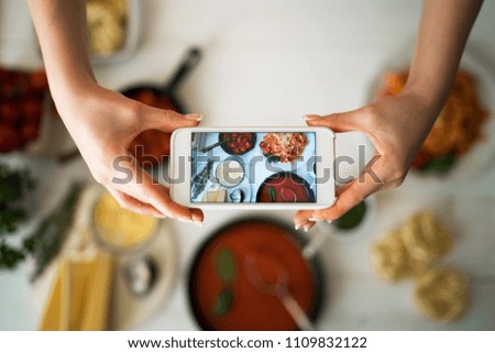 Hands with the smart phone pictures of meal. Young woman, cooking blogger is cooking at the home kitchen in sunny day and is making photo at smartphone. Instagram food blogger workshop concept.
