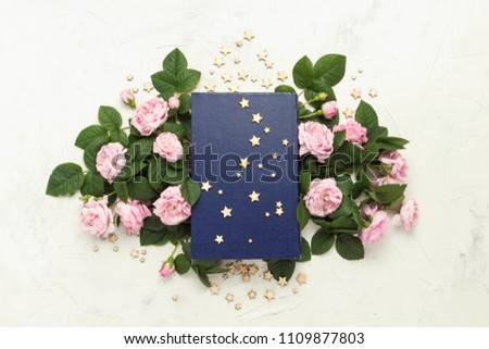 book with a blue cover, small stars and pink roses on a light stone background. Flat lay, top view.