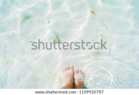 Close-up image of woman's feet on the bottom of the sea near the shore in Cyprus. Light blue transparent water on white sand with sun reflection. Concept of vacation and relaxation, wanderlust