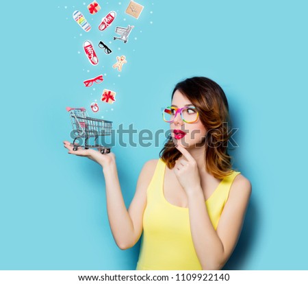 portrait of beautiful young woman with shopping cart on the wonderful blue studio background and with clothes