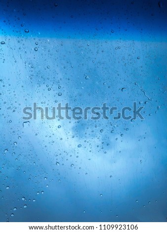Rain drops on front window glasses surface with could, car uv protections film background. Natural pattern of raining day