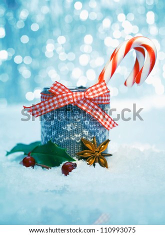 Striped Christmas candy in a rustic container with a checked red and white bow standing in falling snow