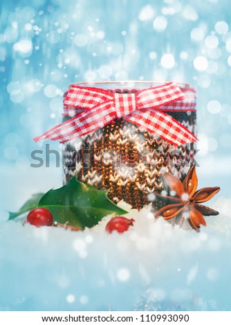 Rustic Christmas still life with a container decorated with a cheerful checked red and white bow with holly and spice nestled in fresh snow