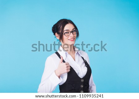 Happy beautiful girl in stylish black glasses showing thumb up symbol on blue background