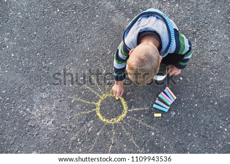 Little boy drawing with a chalk outdoors. Children's picture,creativity on gray dackground road,on asphalt sidewalk.Outside activities for children. top view, copy space. Royalty-Free Stock Photo #1109943536