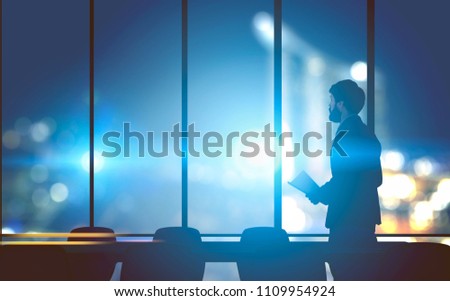 Lonely businessman with papers standing in a modern panoramic windows office. A night cityscape background. Concept of overworking. Toned image double exposure mock up