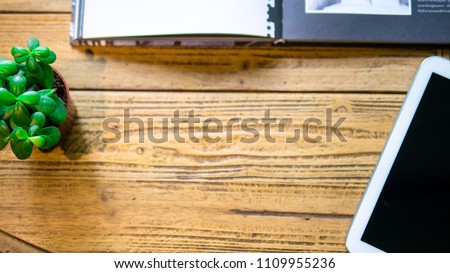 wooden table with a book little green plant white tablet show black screen from top view with copy space.