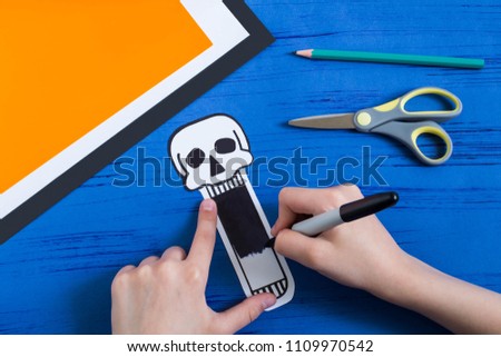 Child makes toothy paper toys (skull and Jack-o'-lantern) for Halloween. Children's art project. DIY concept. Step-by-step photo instruction. Step 5. Color toy with skull