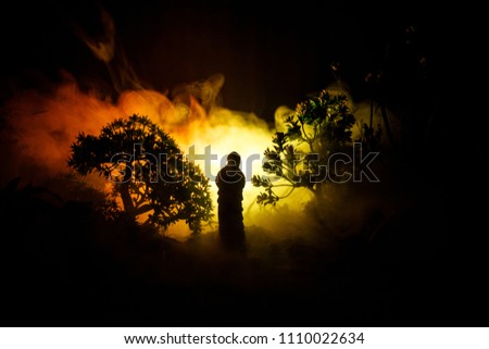 Horror Halloween decorated conceptual image. Alone girl with the light in the forest at night. Silhouette of girl standing between trees with surreal light on background. Selective focus.