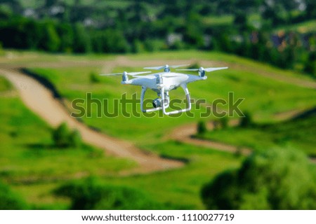White quadcopter with high resolution digital camera for a professional aerial video and photo over green landscape background. Operation of drone in air