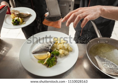 Chef with diligence finishing dish on plate, fish with garnish. Commercial kitchen concept.