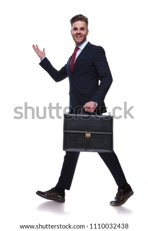 excited walking businessman with suitcase in hand presenting behind on white background, full body picture