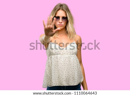 Young woman wearing sunglasses with heart shape annoyed with bad attitude making stop sign with hand, saying no, expressing security, defense or restriction, maybe pushing
