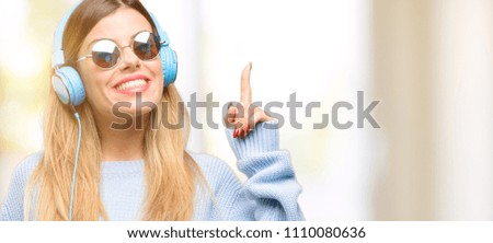 Young woman listen to music with headphone raising finger, the number one