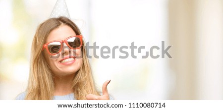 Young woman celebrates birthday smiling broadly showing thumbs up gesture to camera, expression of like and approval