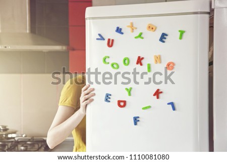 Woman looking in open fridge with Cooking  letters on door. Cooking for family and children concept