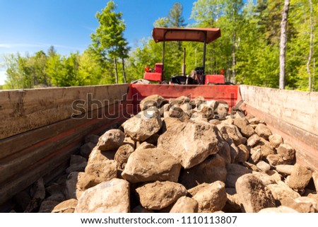 A pile of rocks and stones in the back of a red tractor outside on a sunny day.