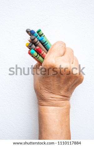 Senior woman's hand holding multicolour crayon  isolated on white background