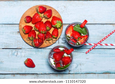 Summer cold drink with strawberries, mint and ice in glass on blue wooden background. Closeup of cocktails with fresh berry fruits.