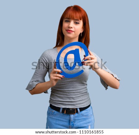 Young redhead girl holding icon of at dot com on blue background