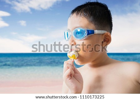 Picture of adorable little boy wearing a swim glasses while eating an ice cream on the beach. Concept of summer vacation