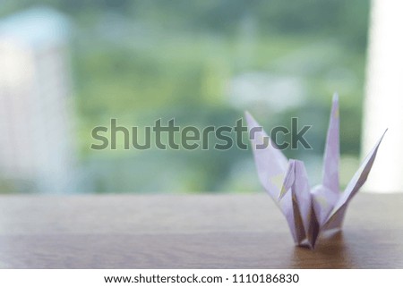 Pink paper crane on wooden table with park background
