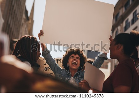 Group of females protesting outdoors on road with a blank banner. Females holding blank sign board during a protest. Royalty-Free Stock Photo #1110245378