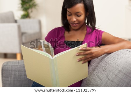 Beautiful youthful African American woman relaxing at home on grey couch wearing pink shirt.