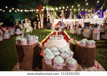 Cakes and cupcakes are placed on the logs at the wedding on a colorful bokeh background.