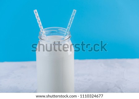 Glass bottle of fresh milk with two straws on blue background. Colorful minimalism. The concept of healthy dairy products with calcium
