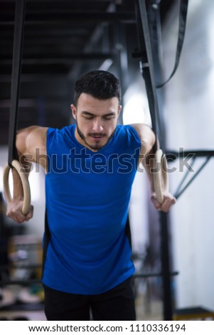 young athlete man working out pull ups with gymnastic rings at the cross fitness gym