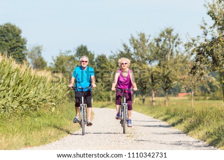 Full length front view of an active senior couple enjoying retirement while riding bicycles in a sunny day of summer in the countryside