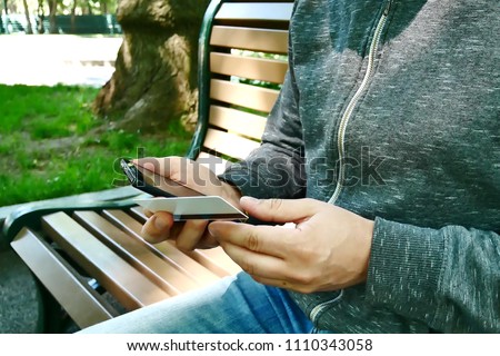 Man Holding Credit or Debit Card Buys in Electronic Store on Internet by Red Phone In Silicone Case Outdoors in City Park On Background Of Bushes With Green Leaves. Shopping Online On Website Or App