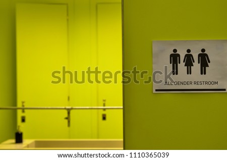 Toilet signage of all kinds next to a bathroom door in acid green with icons of the man, the woman, the transgender. Black icons on a white background.