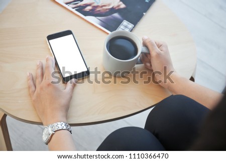 Young woman with cup of coffee holding mobile phone in hand at table indoors