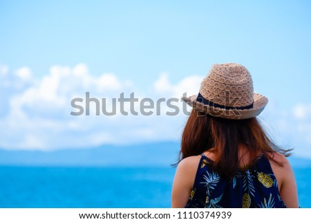Back view of young cute woman that wear a hat is looking landscape of blue sea, sky, mountain and clouds. 
