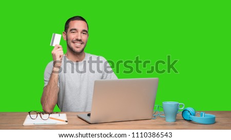 Happy young man sitting at his desk and holding a credit card - Green background