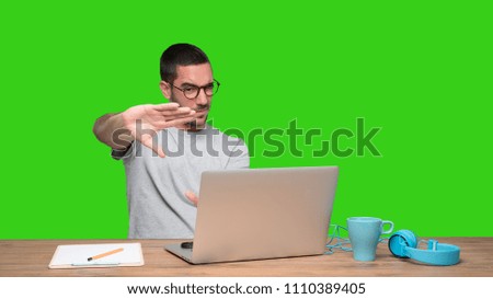 Concentrated young man sitting at his desk doing a gesture of focusing with his hands - Green background