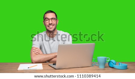 Happy young man sitting at his desk and winking an eye - Green background