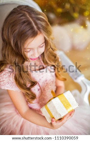 Beautiful little girl in pink dress holds in hand Christmas gift