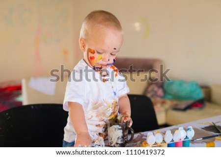 Beautiful little blonde boy, has happy fun smiling face, brown eyes, white t-shirt. Painted brushes water colors in skin. Child portrait. Kids concept hobby.