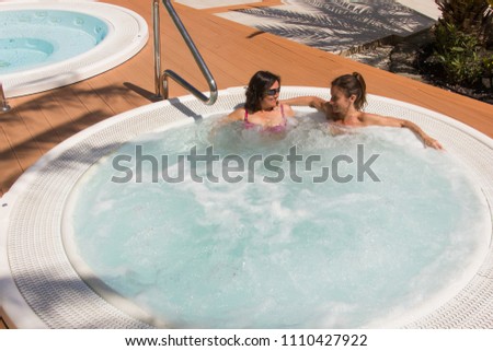 Young women enjoying pool in summer time. Girl friends chat while resting in hot tub. Luxury vacation concept